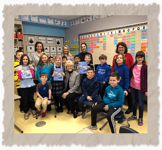 Ilona E. Holland with kids in a classroom holding The Lost Locket of Lewes book